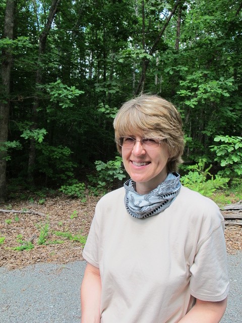 Photo of ARMN member Susan Berry wearing a blue bandanna standing in front of the woods