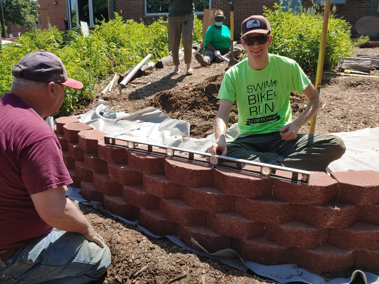 Two volunteers work on building a brick colored wall